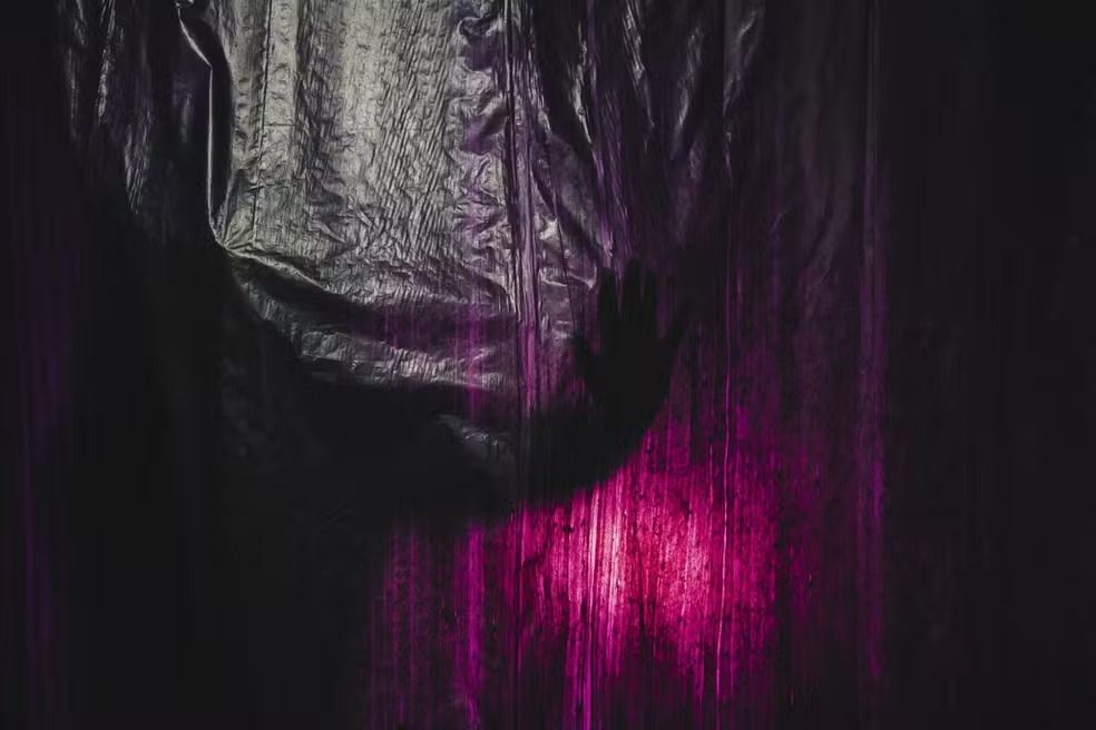 Sala da exposição “Fora de Vista”, revestida por plástico preto, com névoa e iluminação roxa.